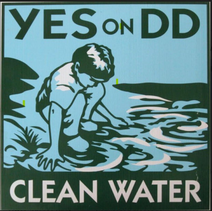 Campaign poster in green, blue, and white. Top text reads "Yes on DD," bottom text "Clean Water." Between the text, a child squats on the lake shore and touches the water.